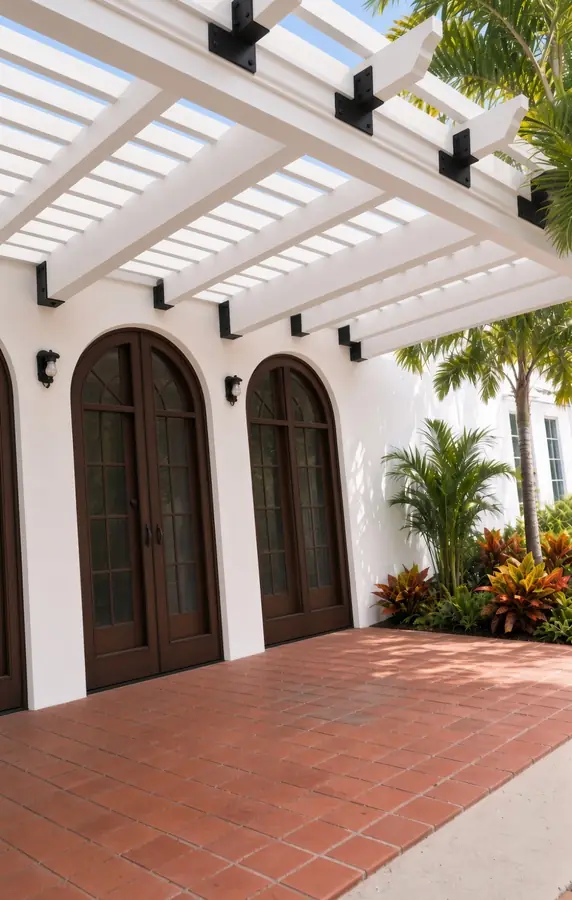 AI concept rendering of a white pergola over a terracotta tile patio beside tall arched wood doors and tropical plants