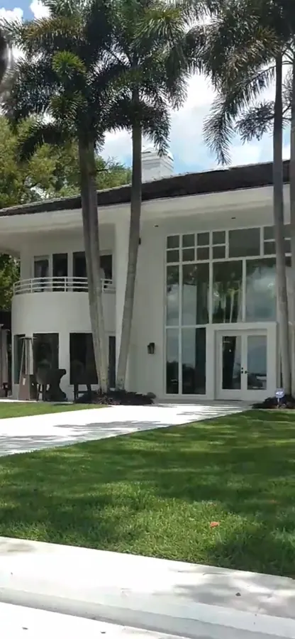 White modern home with a curved balcony, tall glass windows and palms above a green lawn and white steps