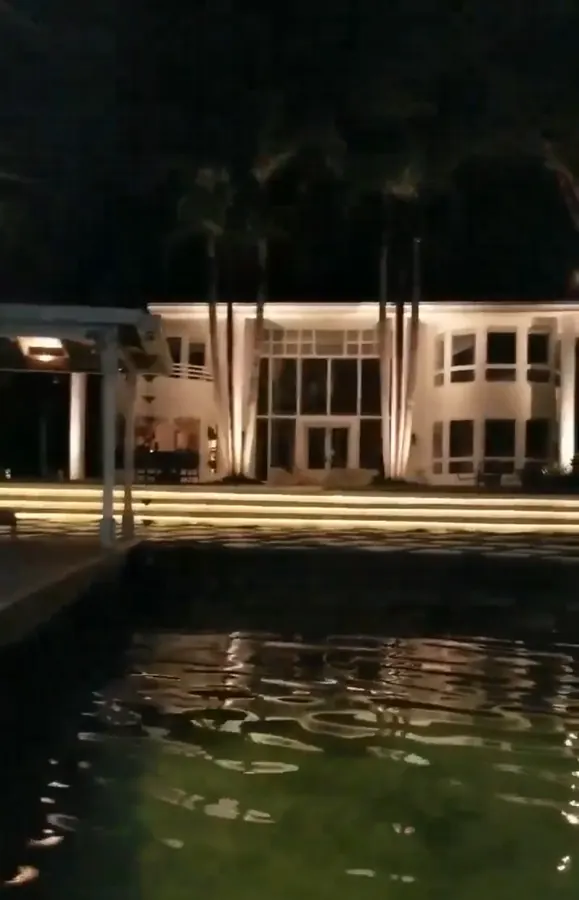 White modern waterfront home uplit at night, seen across the water with lit steps along the shore