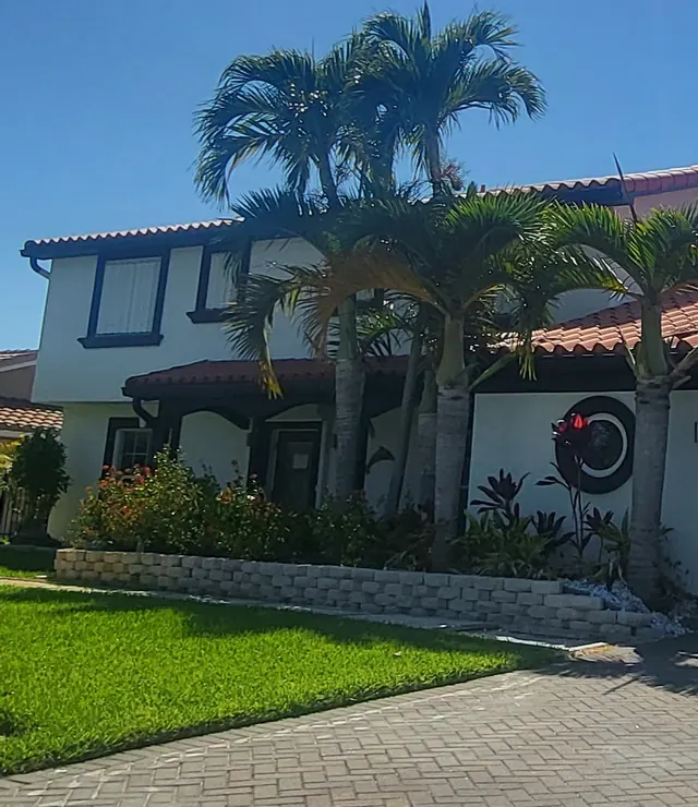 White stucco home with a red tile roof and palm trees above a brick paver driveway
