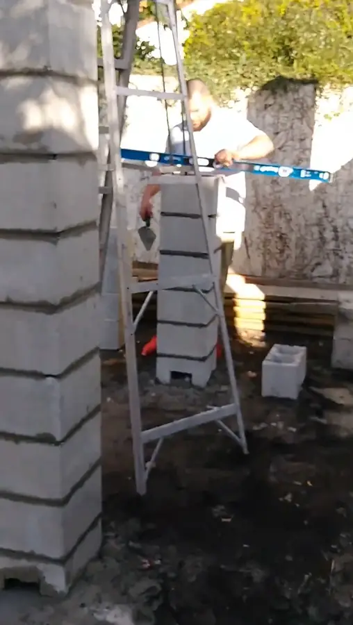 Concrete block columns going up beside an aluminum ladder while a crew member checks a level, Winter Park, 2017