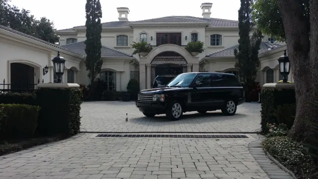 Black Range Rover parked in the paver motor court of a cream stone estate with lanterns on the gate piers