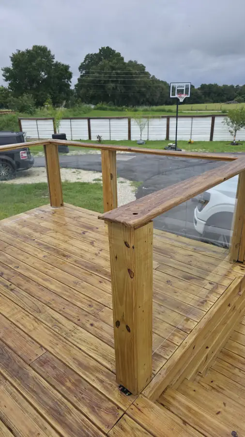 Corner of the finished pressure-treated deck with wood posts and top rail, looking out over a lawn and trees