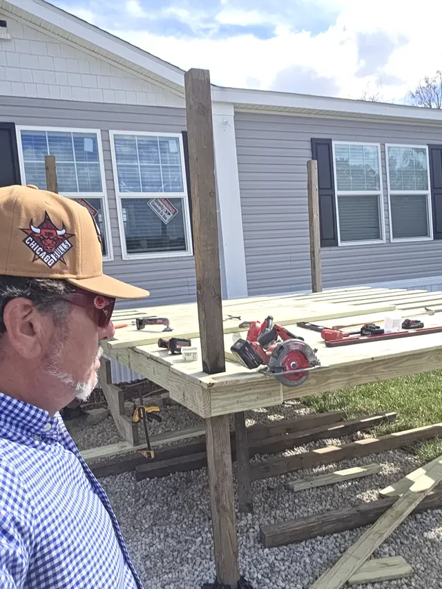 Man in a Bulls cap and blue checked shirt beside a new pressure-treated deck platform with saws and tools on it