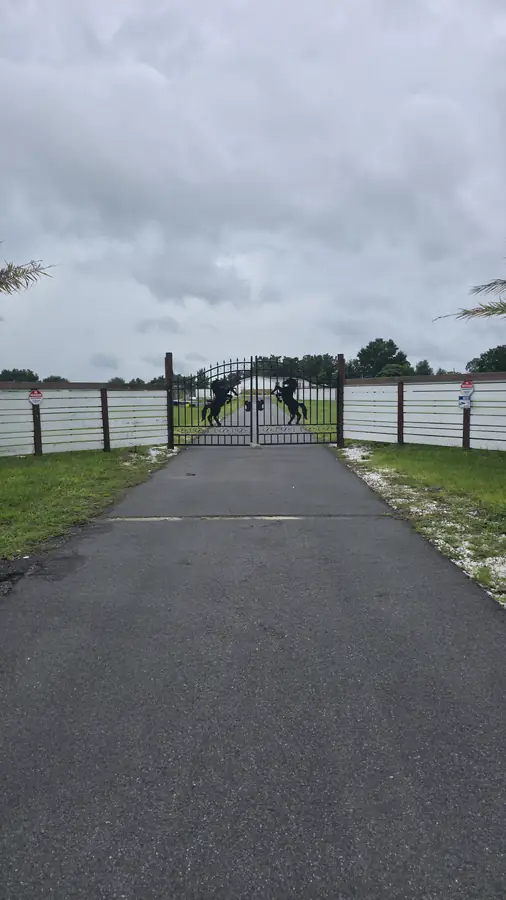 Paved driveway leading to the installed black iron entry gate set in a white fence line under a cloudy sky