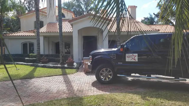 Black Ford F-250 with a Red Star door sign parked on a brick paver drive at a white home with a red tile roof