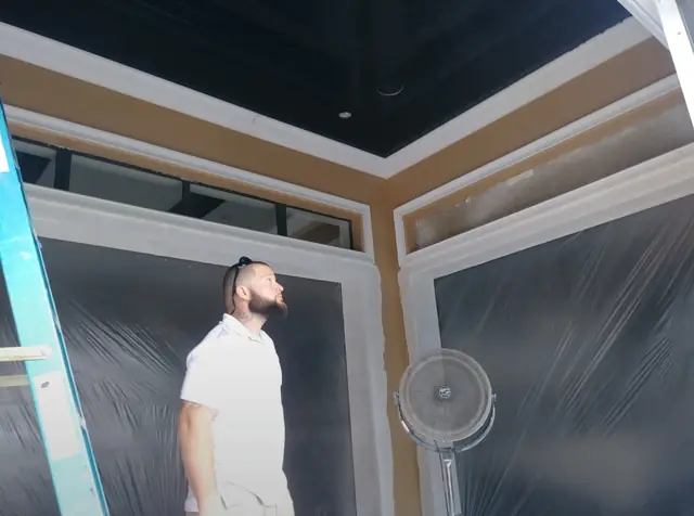 Pool room interior with a new black ceiling and trim, windows masked in plastic, man standing in the room, Winter Park, 2017
