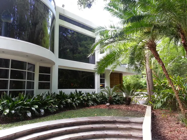 White modern home with curved glass walls, tropical plantings, palms and wide curved stone steps