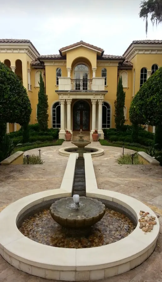 Yellow Mediterranean estate with a columned entry, a long runnel and two tiered stone fountains in a travertine courtyard
