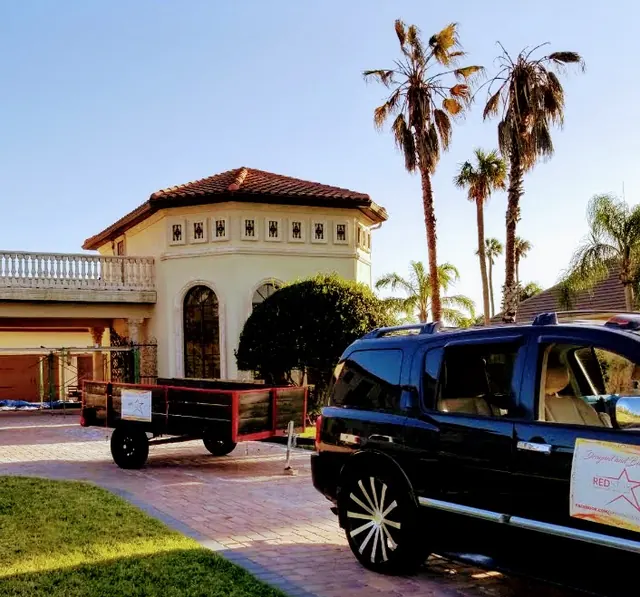 Black SUV with a Red Star sign on the door and a wood-sided work trailer parked on a brick drive at a Mediterranean-style estate